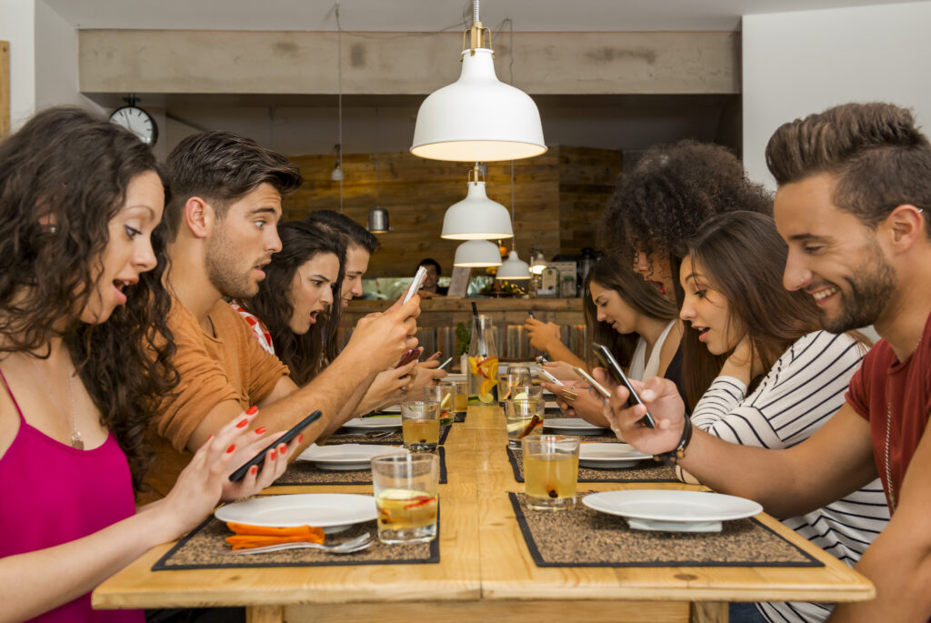 An image show a group of people sit on same table and all using their phones.