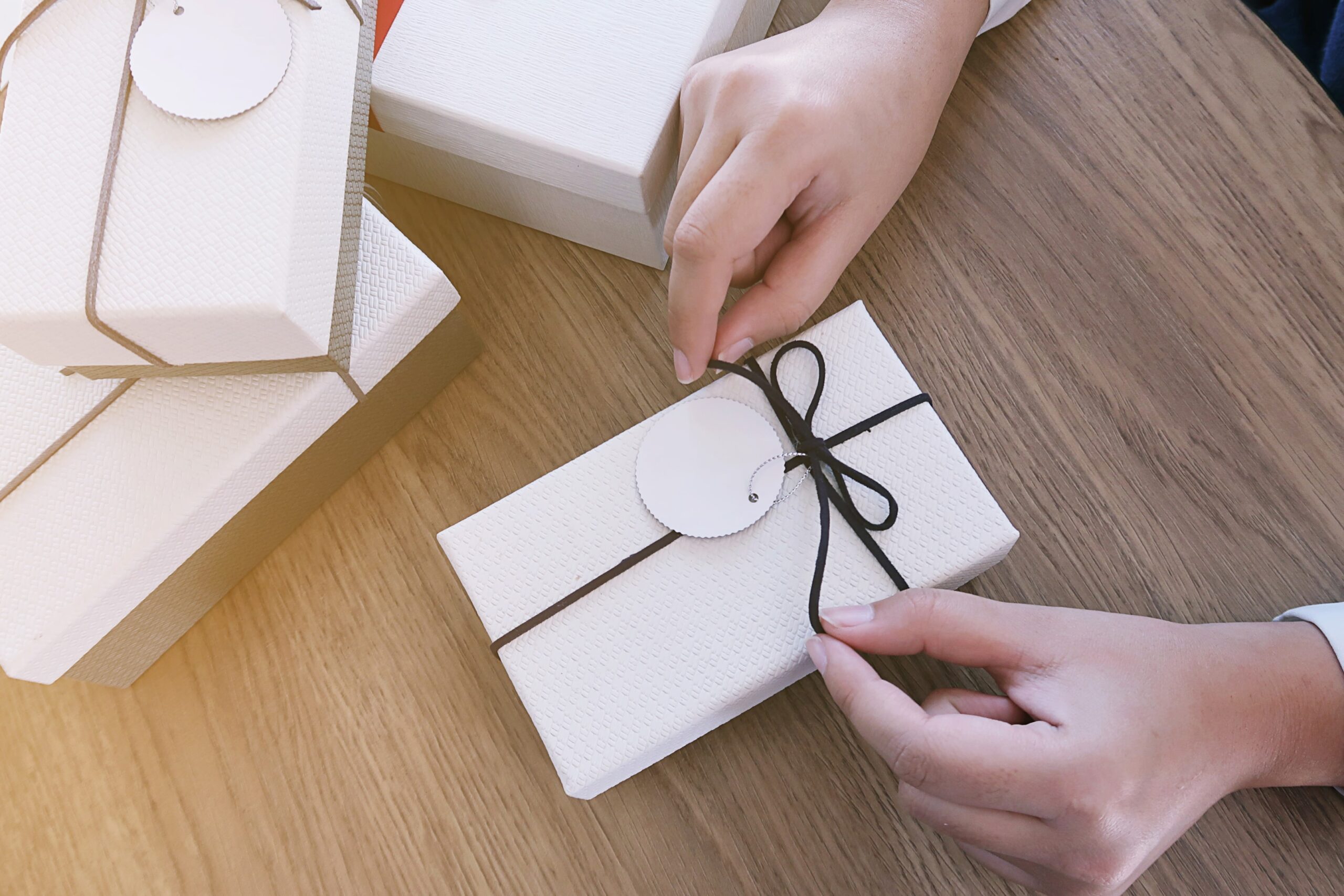 Hands unwrapping a luxury gift box with a handwritten tag, representing a personalized client experience that sparks word-of-mouth referrals.